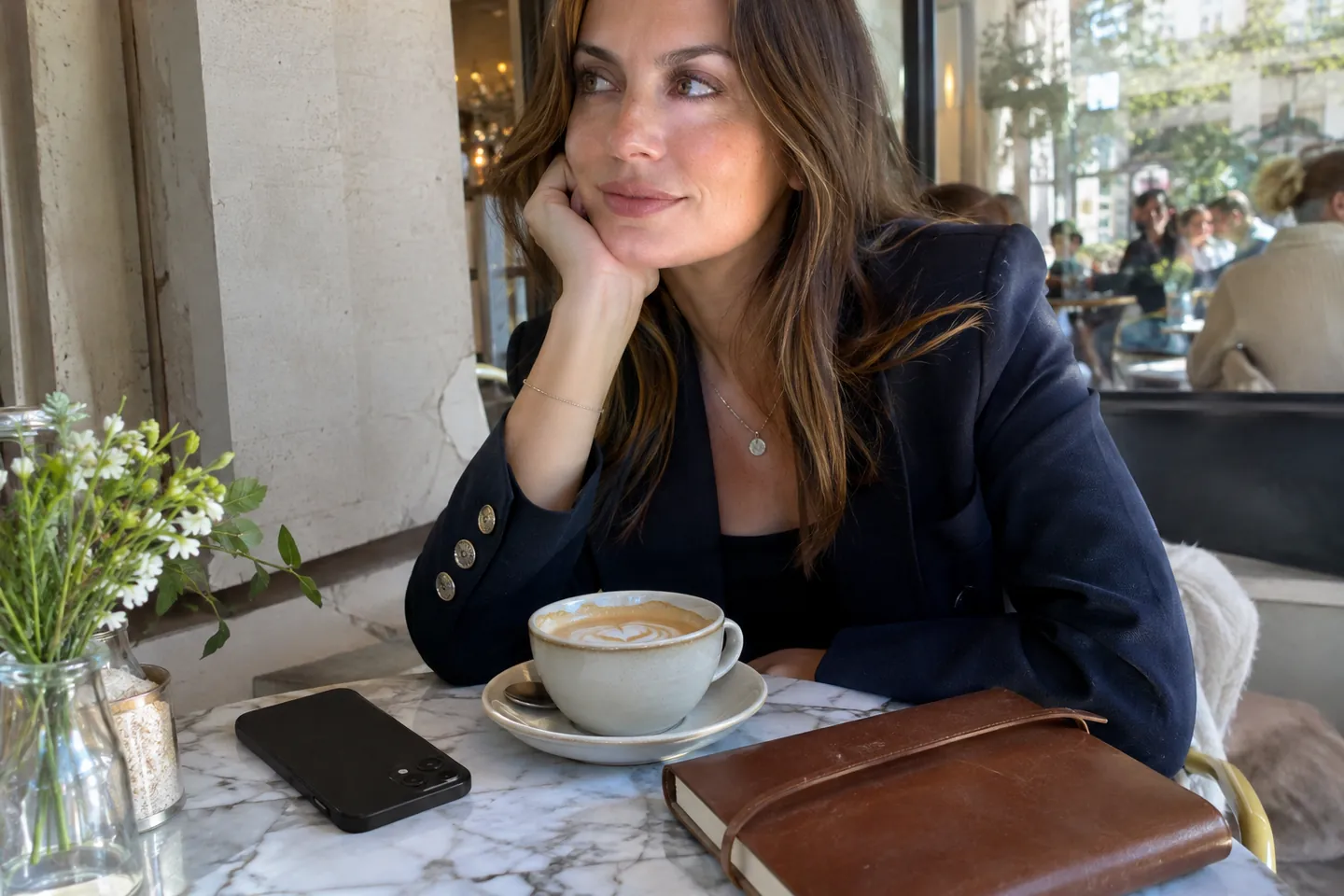 A woman in a navy blazer at a café table with a latte and a phone face down