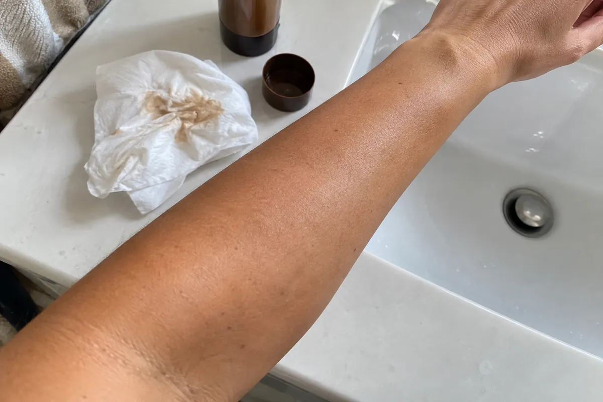 A forearm after a self-tan application with a tissue on the sink edge